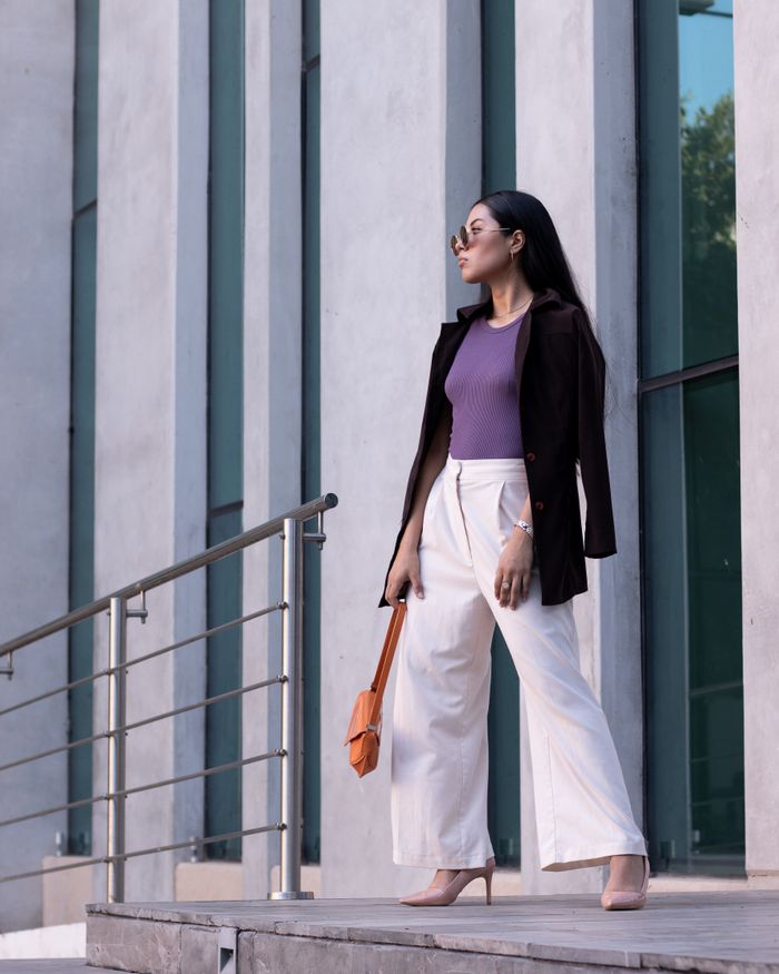 Confident woman in fashionable attire standing on steps outside an urban office building.